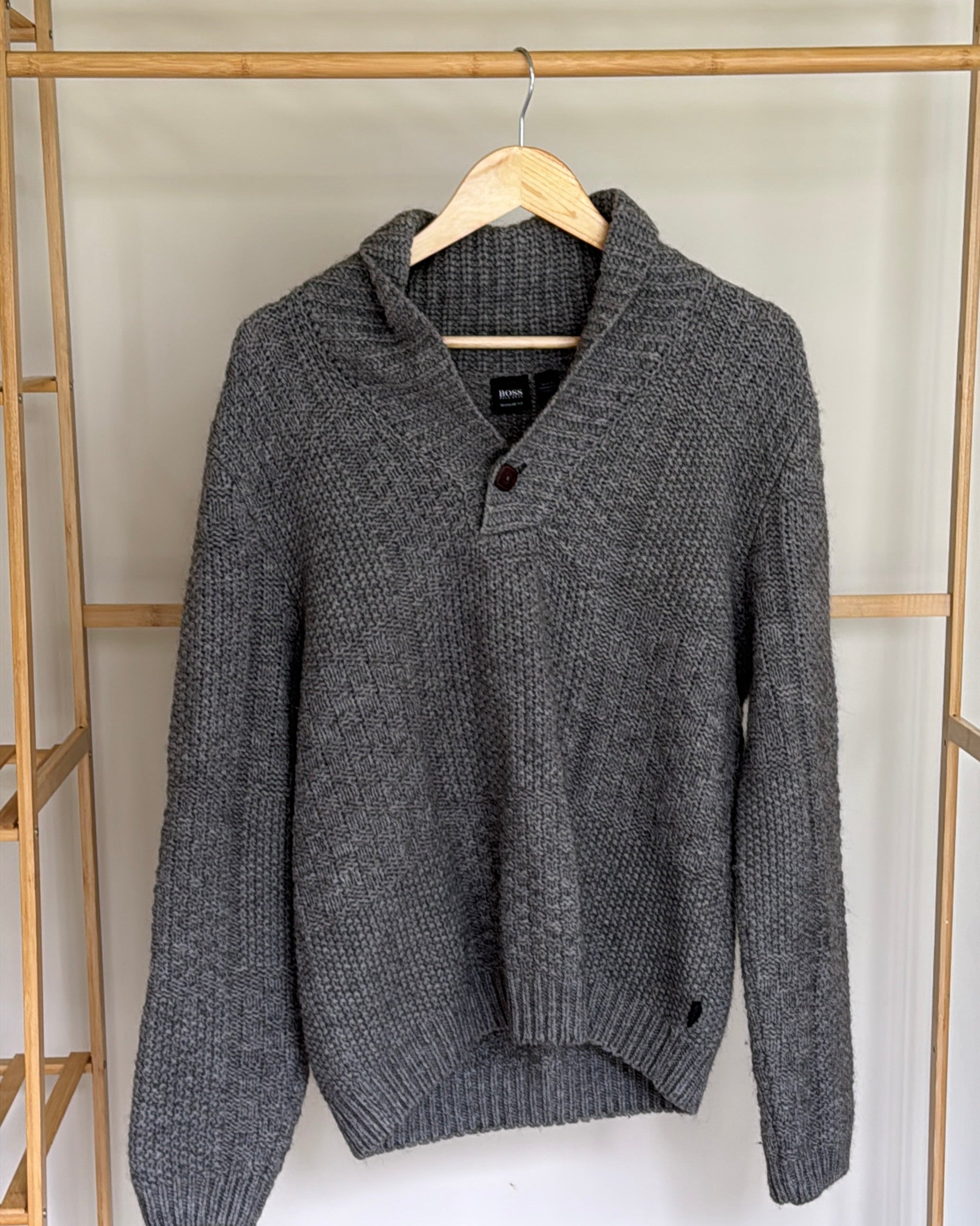 Gray sweater on a hanger against a white wall with wooden shelves.